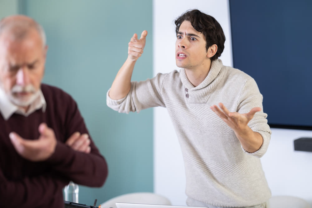 Young man scolds elderly man in office