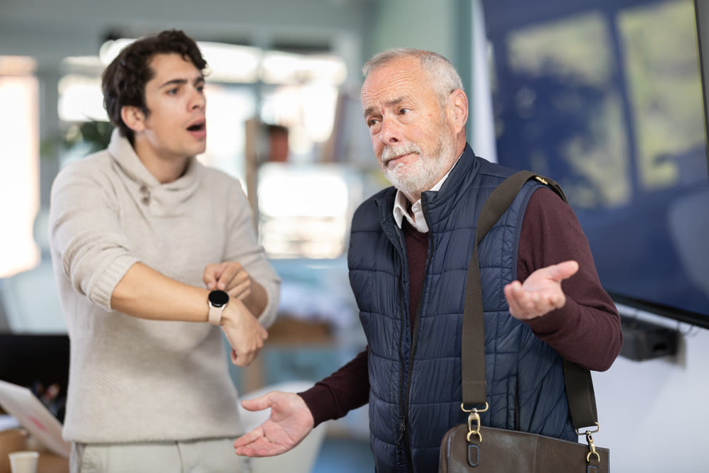 Young man scolding elderly male colleague for being late to office