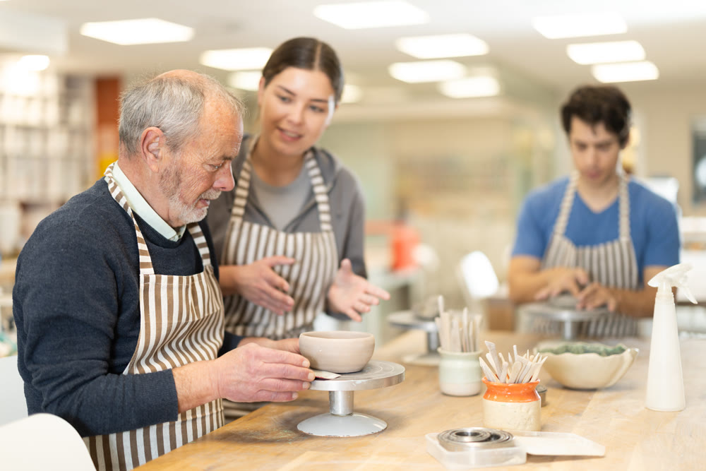Young woman helping eldery man sculpting ceramic piece