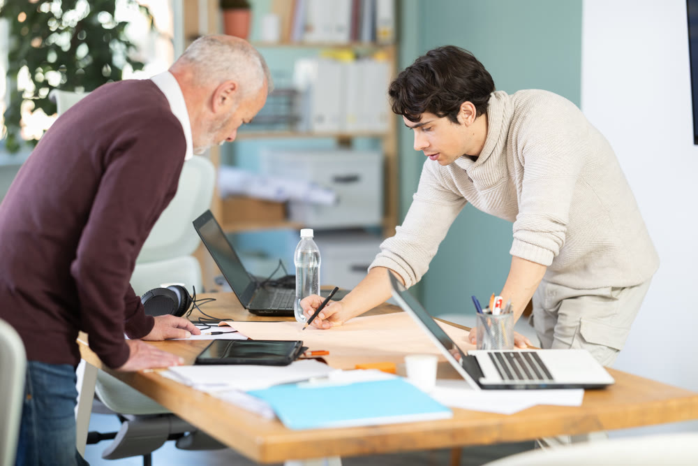 Young and elderly men colleagues discussing building plan in office