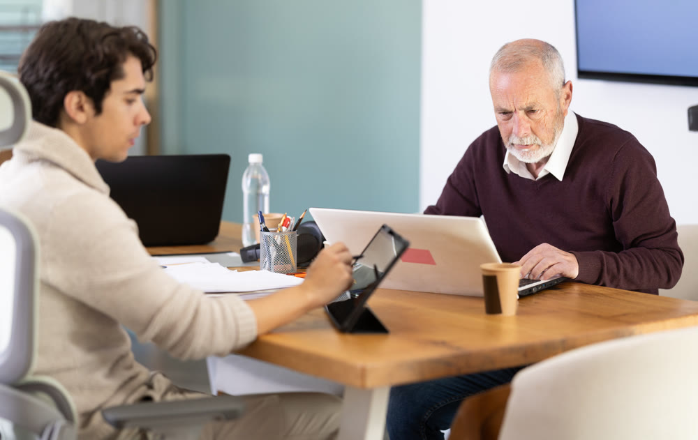 Young man working on tablet and elderly man on laptop in office