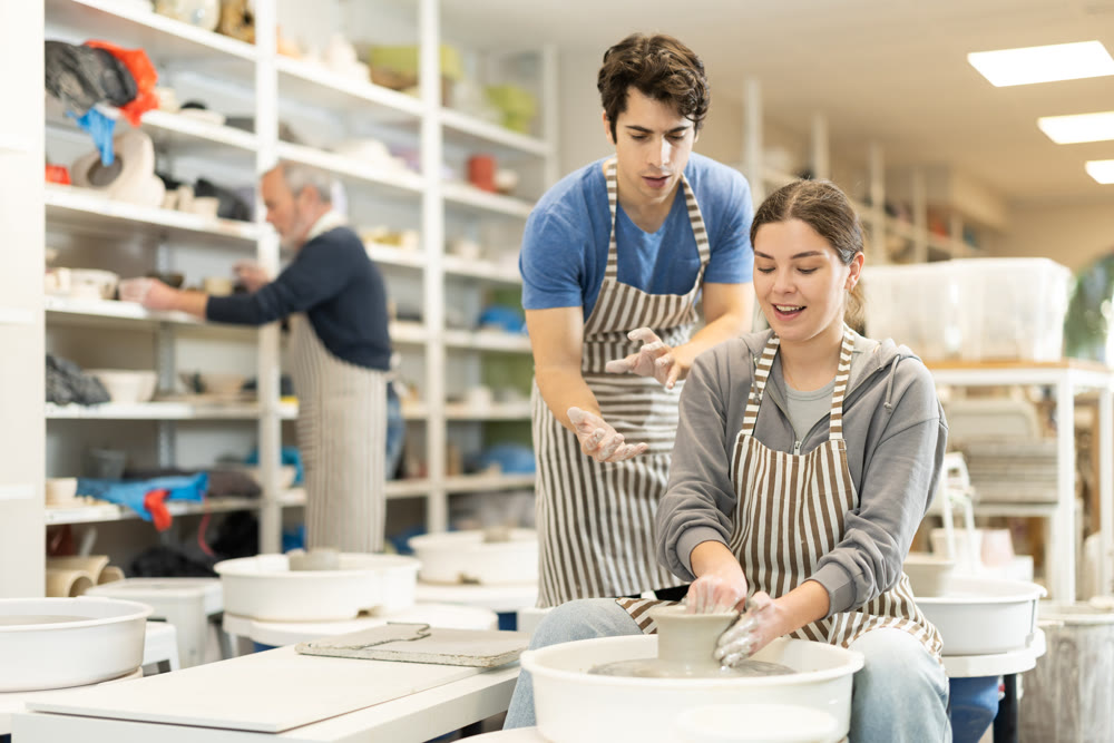 Young man helping young woman shape pottery on wheel