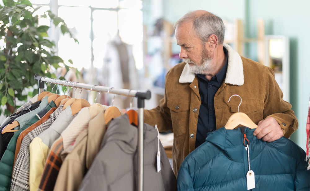 Mature male shopper chooses and tries fashionable down jacket in clothing store