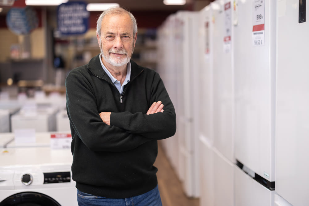 Elderly man choose modern fridge at supermarket