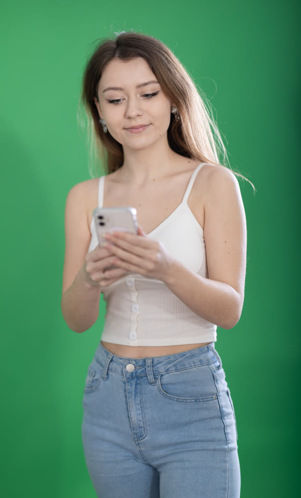 Chroma key compositing. Pretty young woman scrolling through smartphone screen against green screen background