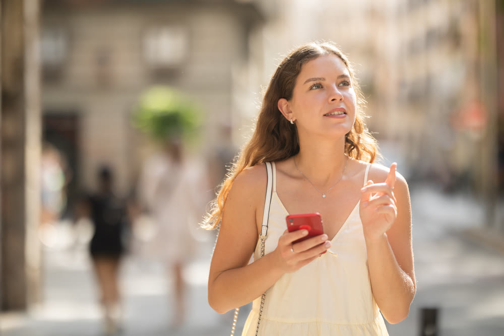Young woman with phone walking along city street