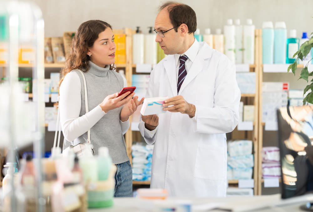 Female customer scans QR code on package of paracetamol. Pharmacist helps her