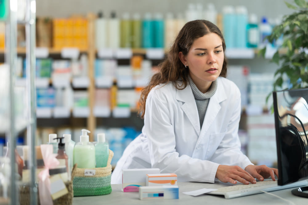 Portrait of young female pharmacist working at computer in pharmacy