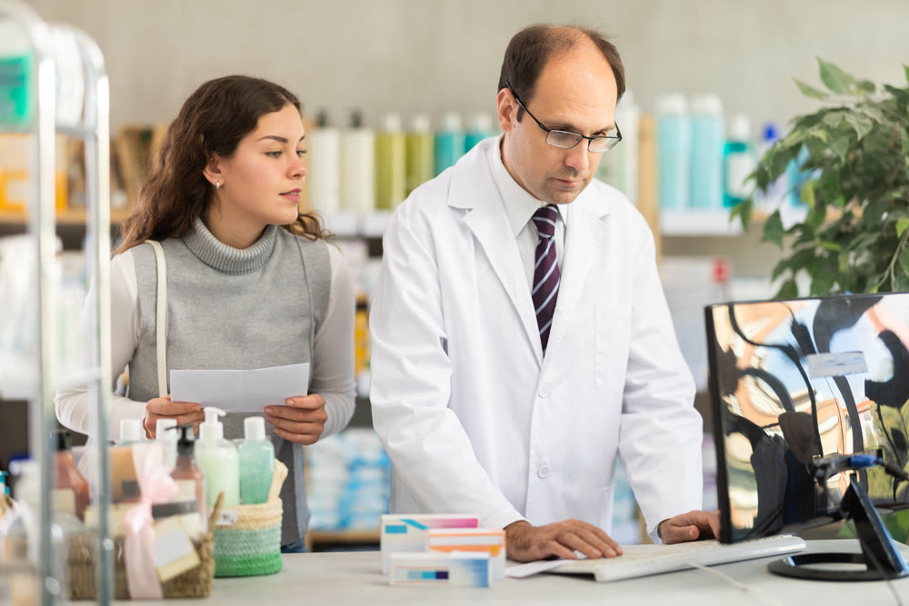 Male pharmacist and female customer search for drug name online together