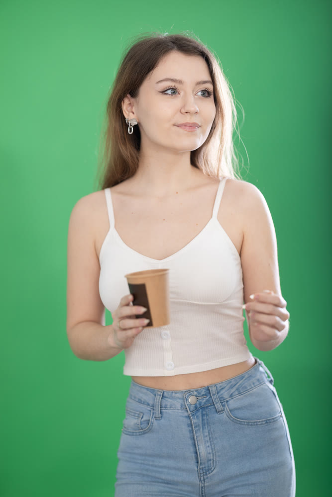 Young woman drinking coffee in front of green screen