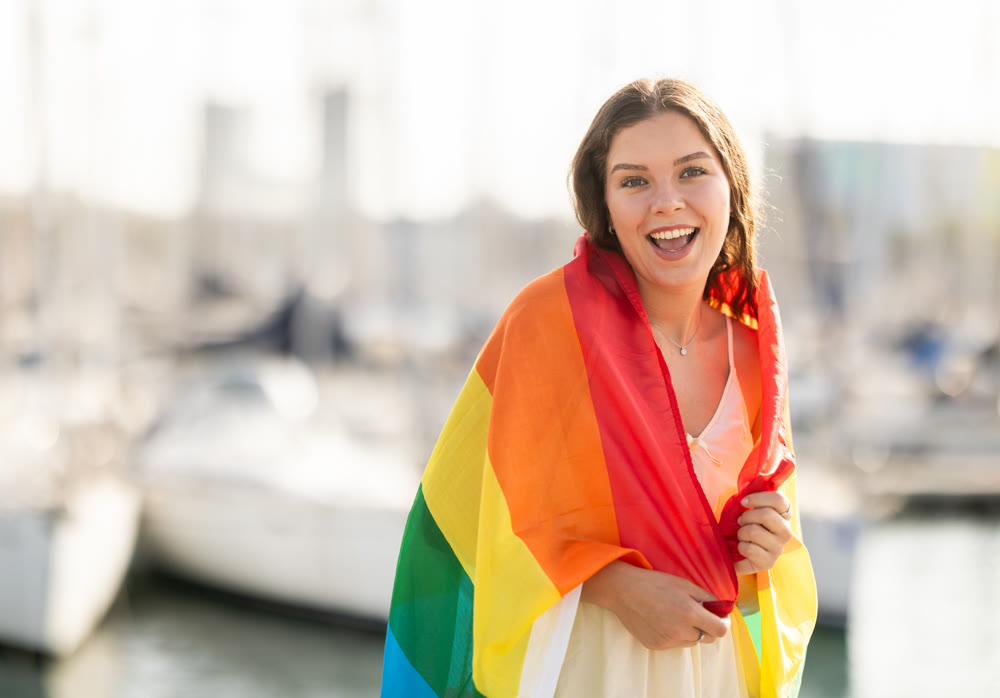 Happy girl waving LGBT flag against seaport and yachts
