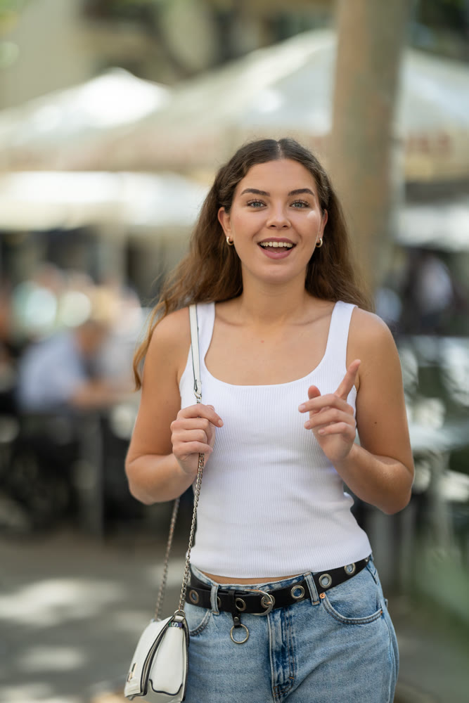Happy young woman walking past street cafe on summer day
