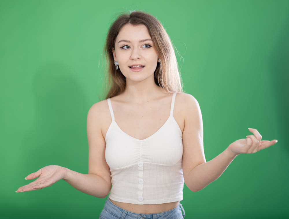 European woman stands on a green background and says
