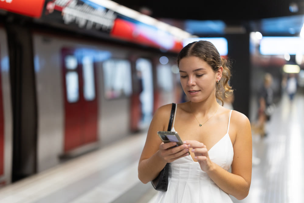Young girl standing on metro platform with phone in hand