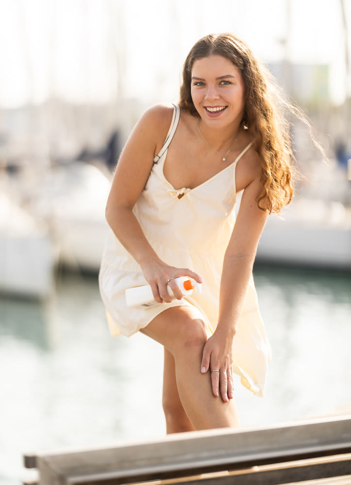 Young woman applying sunscreen on bench near port