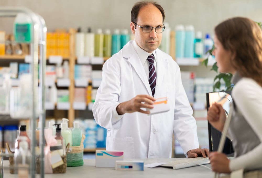 Experienced male pharmacist helping girl choose medicines in pharmacy