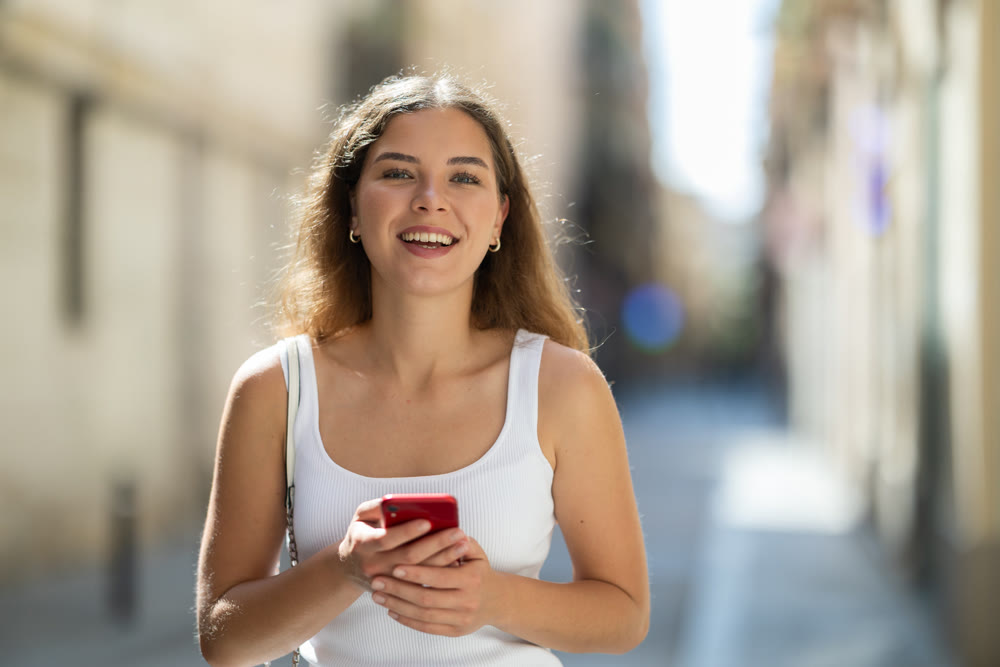 Young woman checking phone while walking in summer city