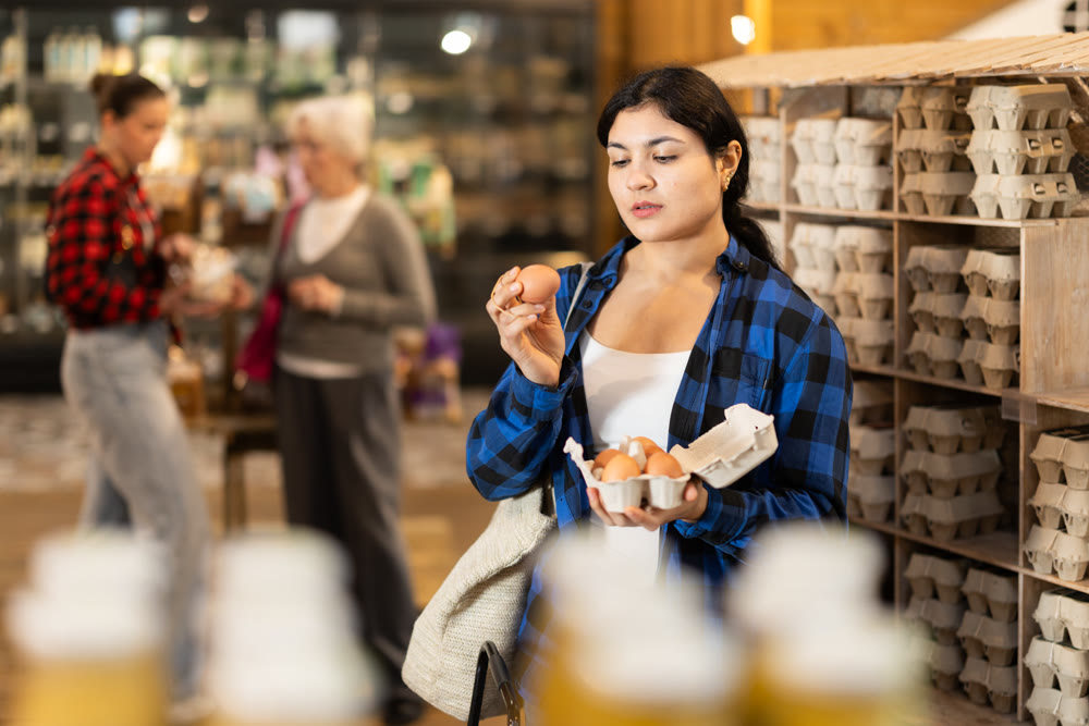 Young woman choosing eggs at grocery store