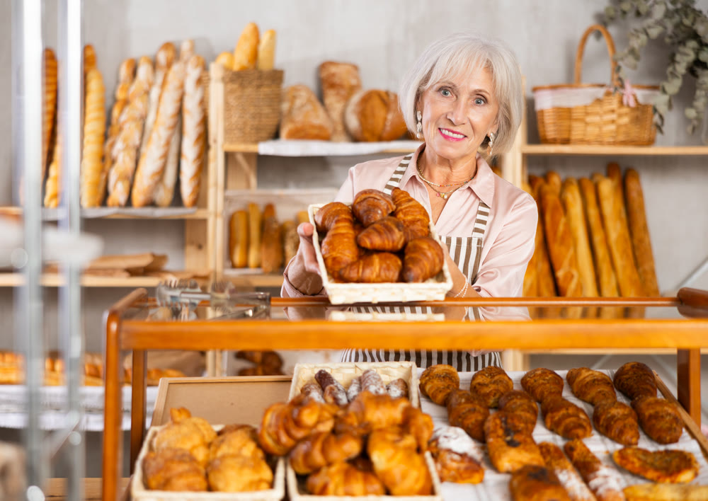 Elderly bakery saleswoman places fresh croissants on display