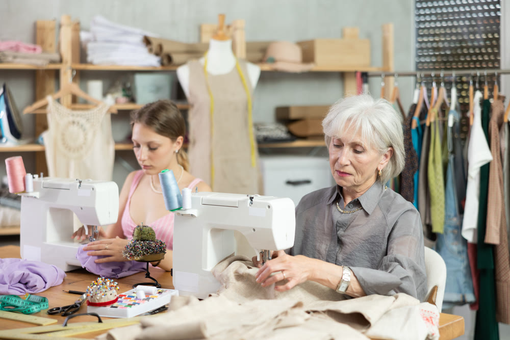 Two female dressmakers working with sewing-machine in tailor's workshop
