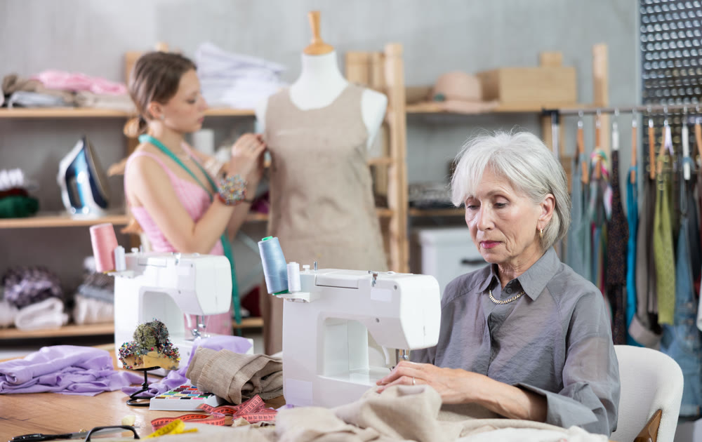Mature tailoress using sewing-machine while other working with mannequin