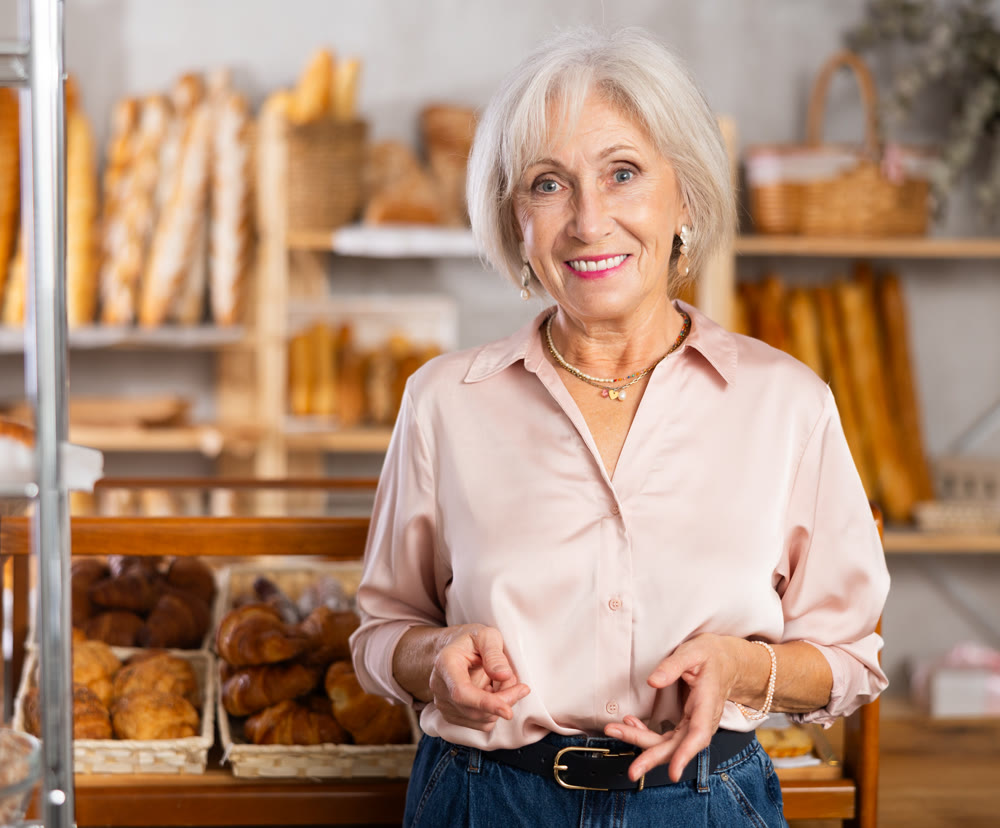 Mature European woman near window of bakery food court store examines assortment