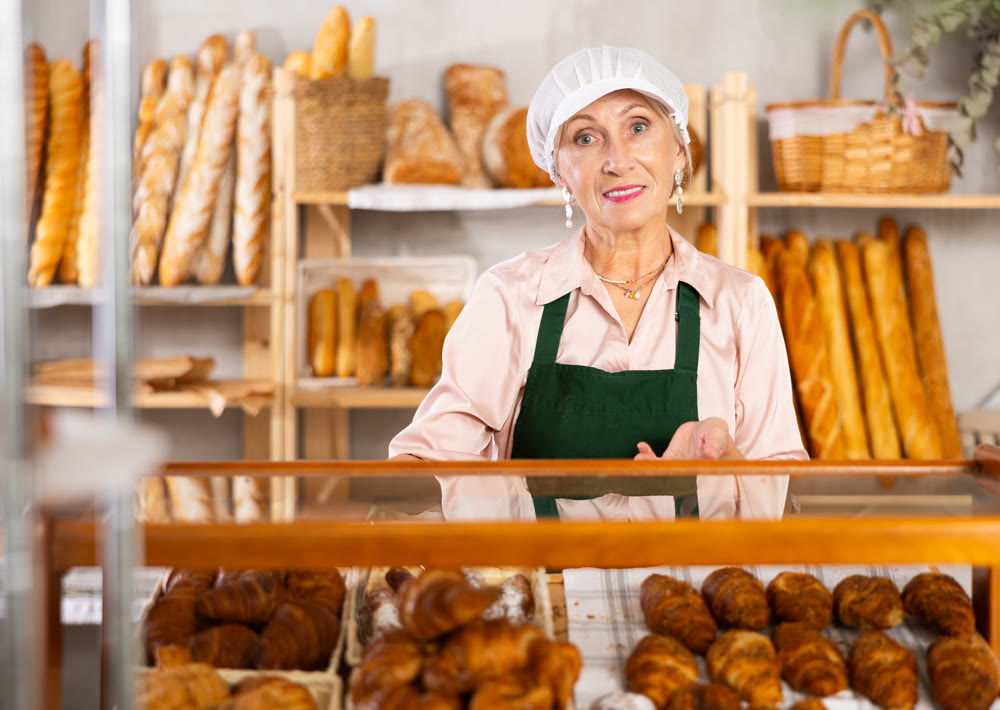 An elderly baker's worker sells croissants and displays a variety of different types of crescent-shaped buns.