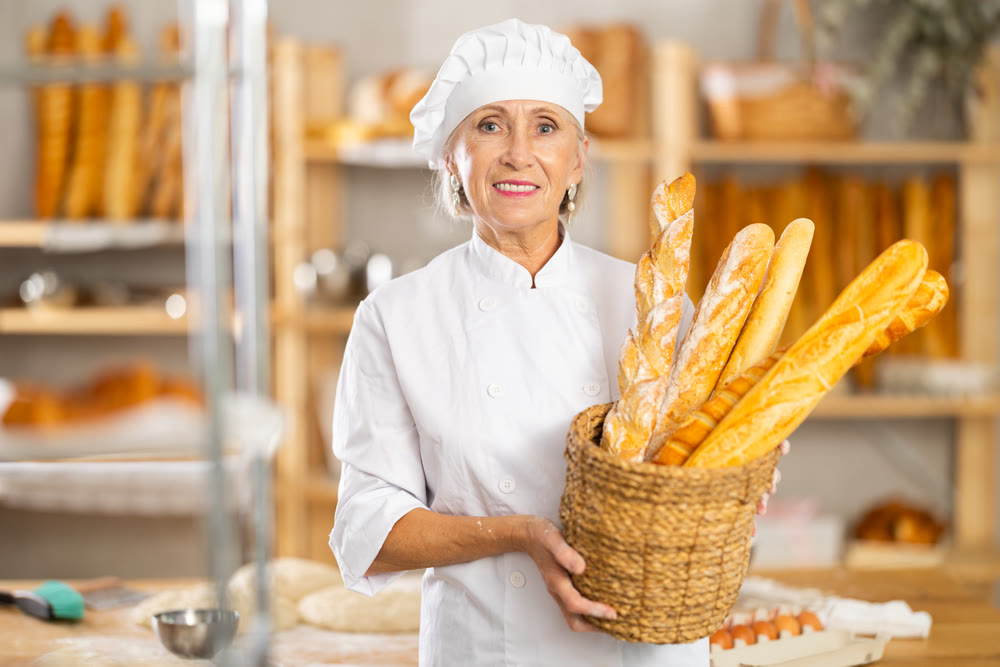 Senior female baker worker shows baguette