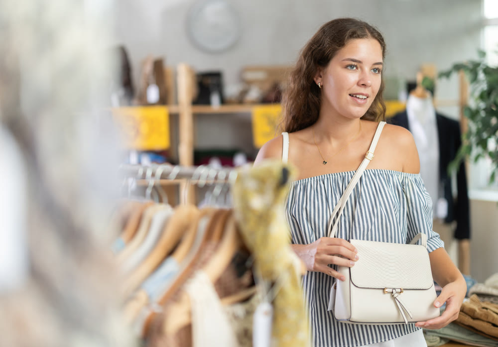 Happy young woman choosing handbag in clothing store