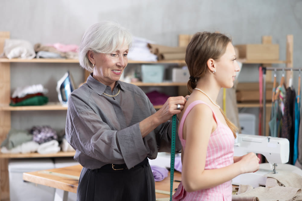 Elderly seamstress takes body measurements from young woman