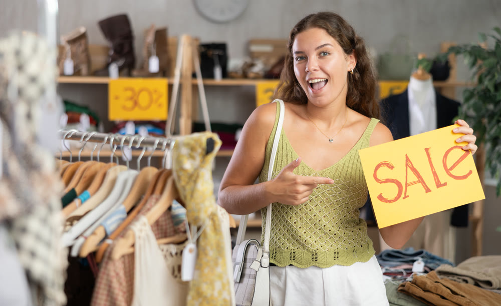 Young woman holding sale sign in clothing store