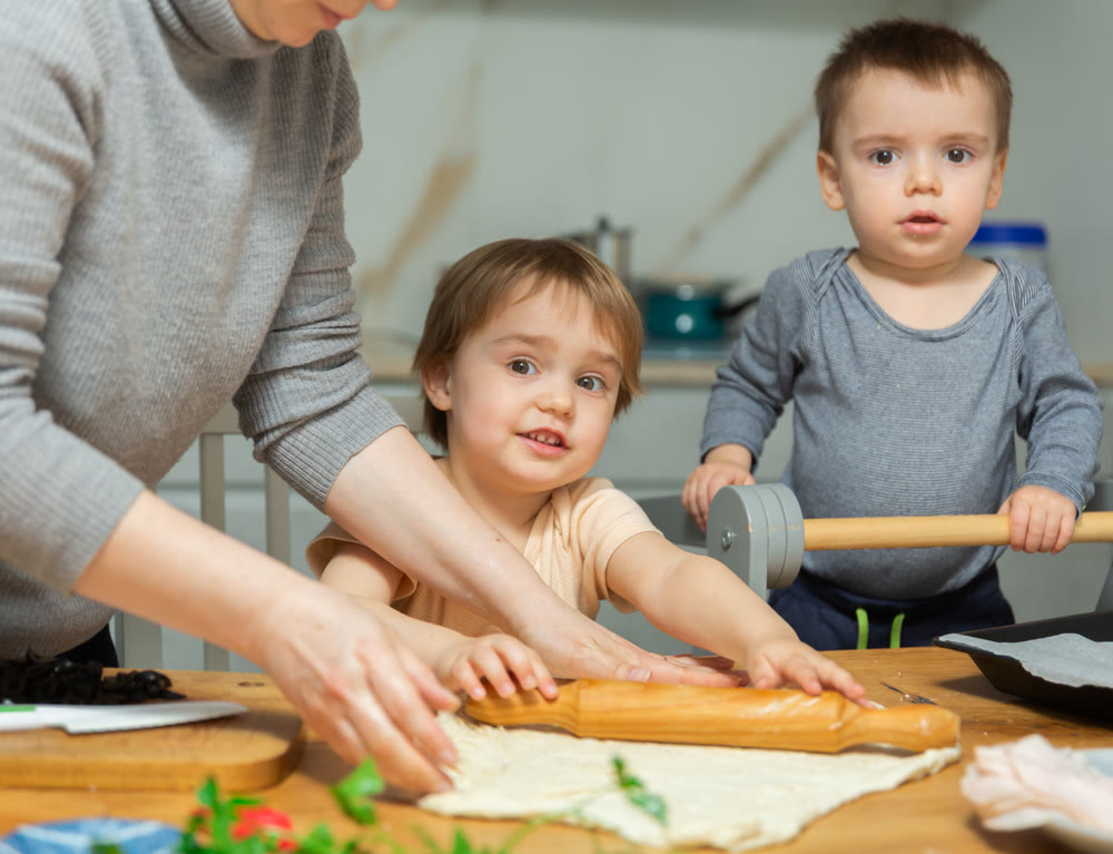 Family are cooking pizza together in cozy home kitchen. Cute kids with happy mother are preparing food or meal for dinner