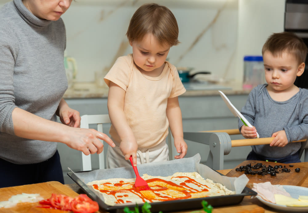 Mother and two young boys making pizza together in home kitchen