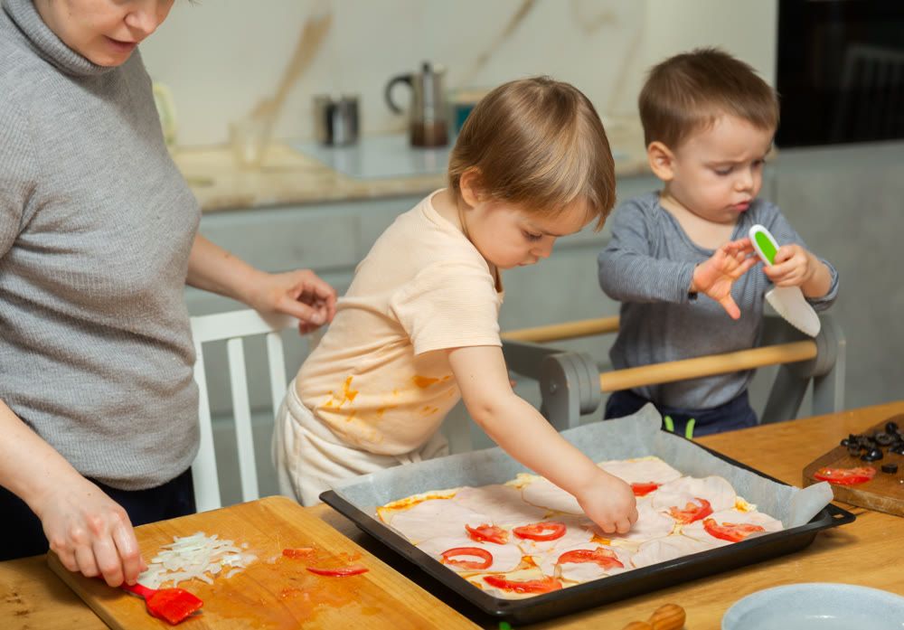 Mother and two young boys making pizza together in home kitchen