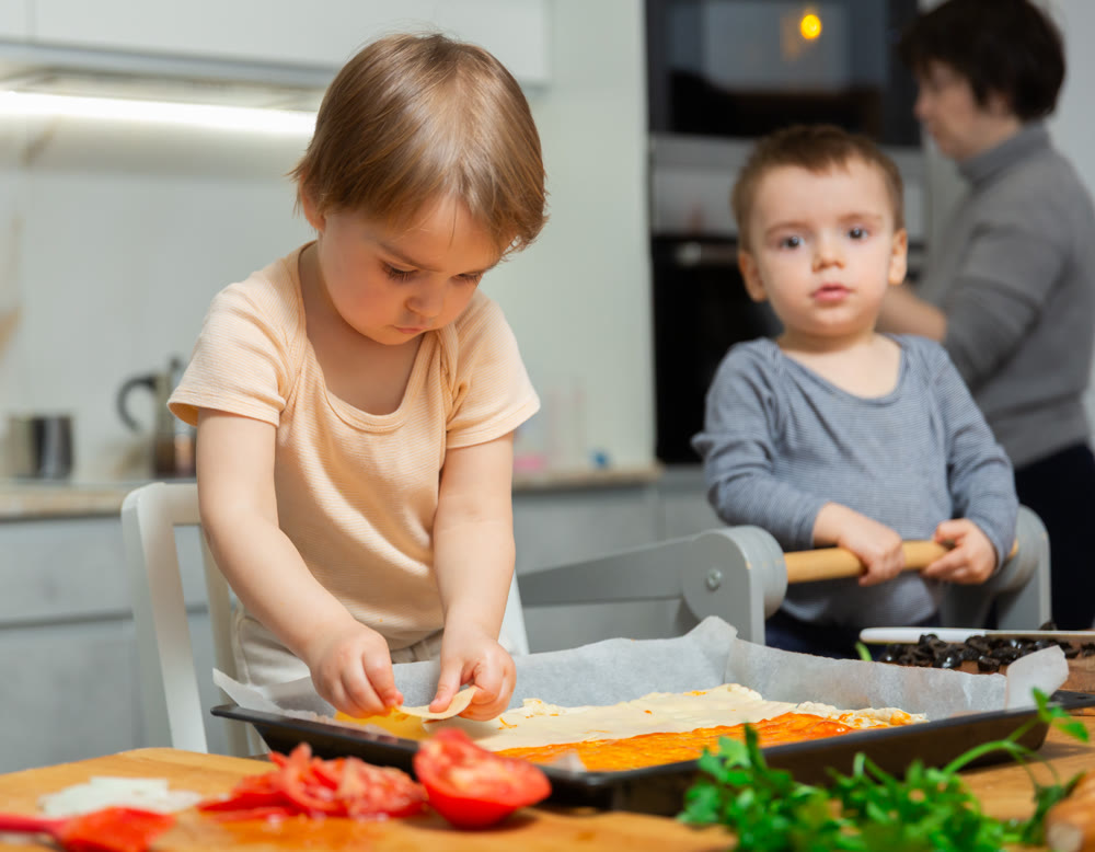 Mother and two young boys making pizza together in home kitchen