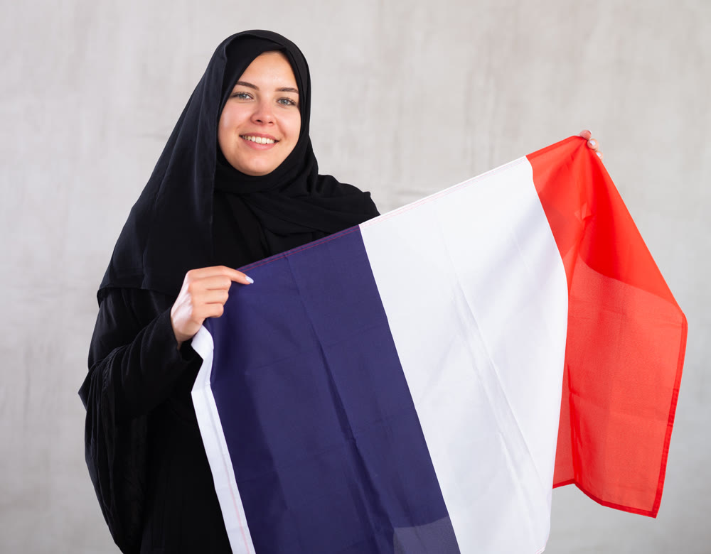 Balanced smiling Muslim woman in traditional black hijab holds flag of France