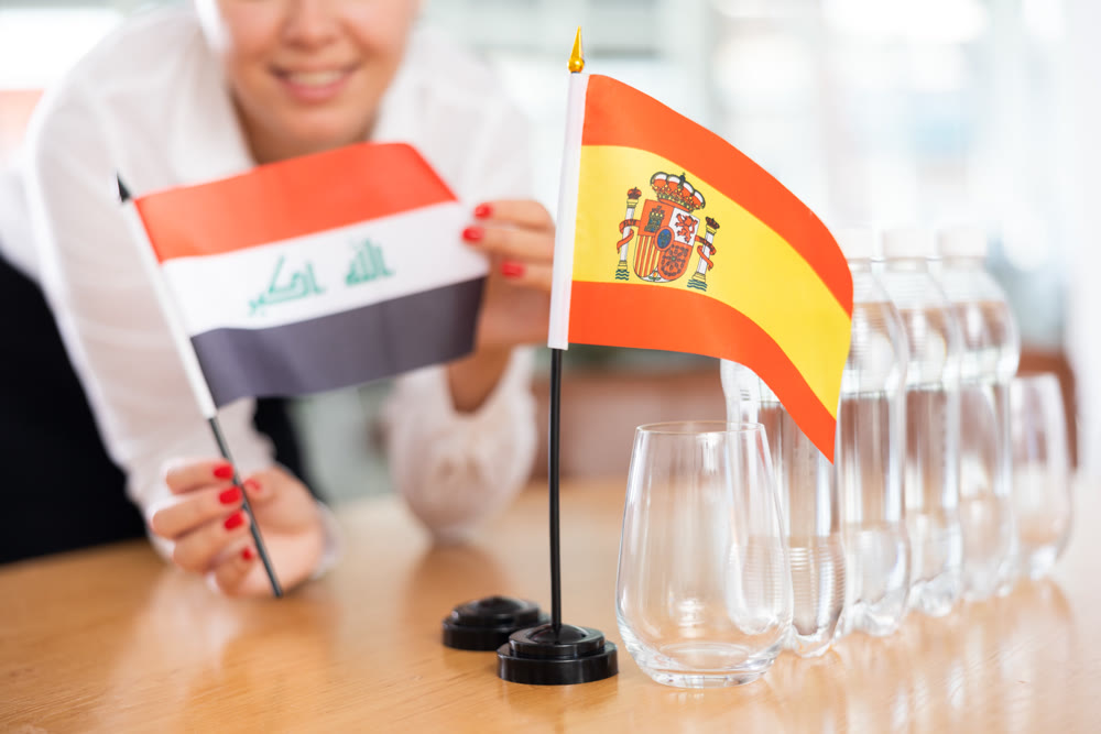 Young woman putting flags of Iraq and Spain on table in office