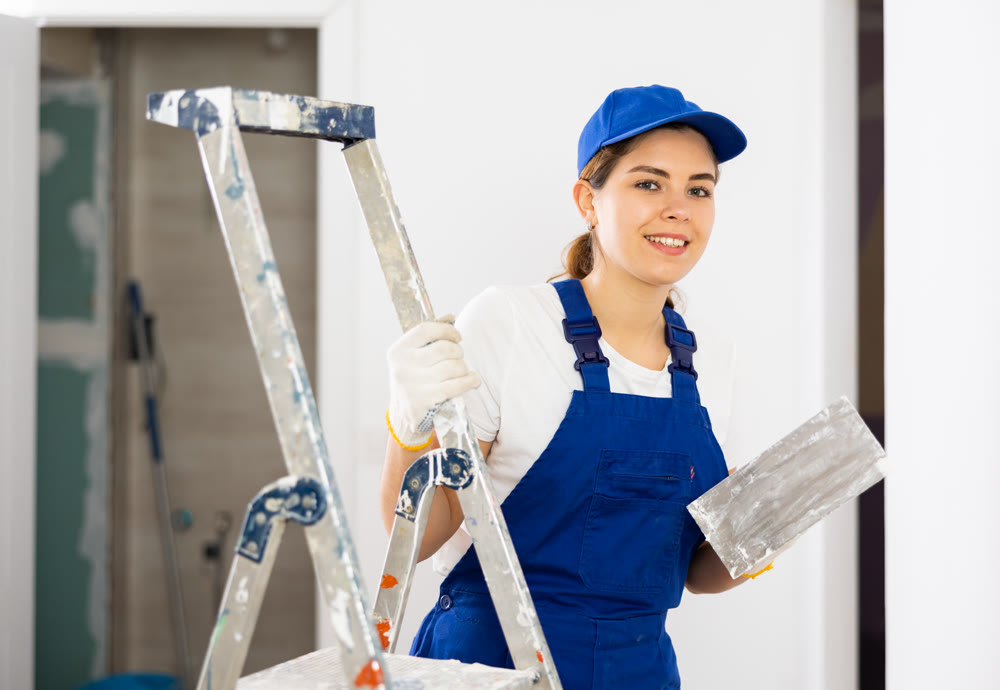 Portrait of young woman builder with trowel standing in apartment