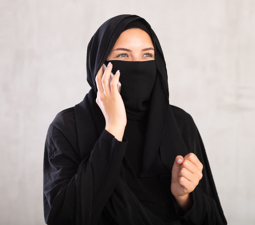 Young woman dressed in traditional islamic clothes with her face covered having phone conversation