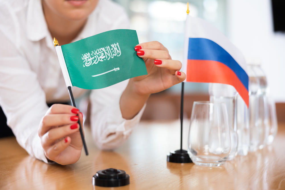 Flags of Saudi Arabia and Russia stand on negotiating table in office