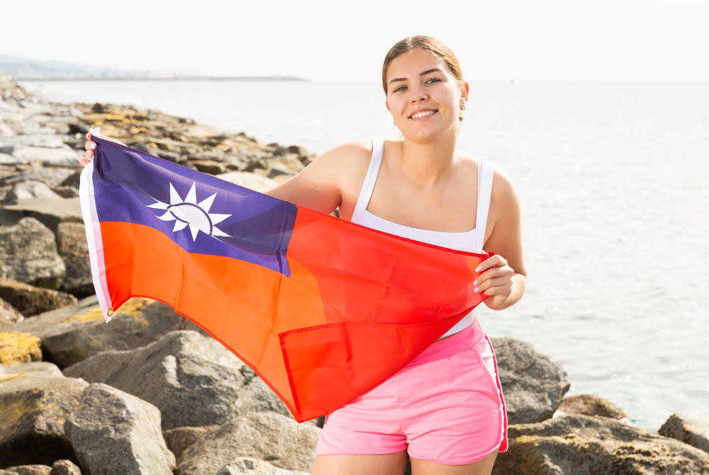 Enjoying vacation in Taiwan. Young woman with national Taiwanese flag on the seashore on sunny day