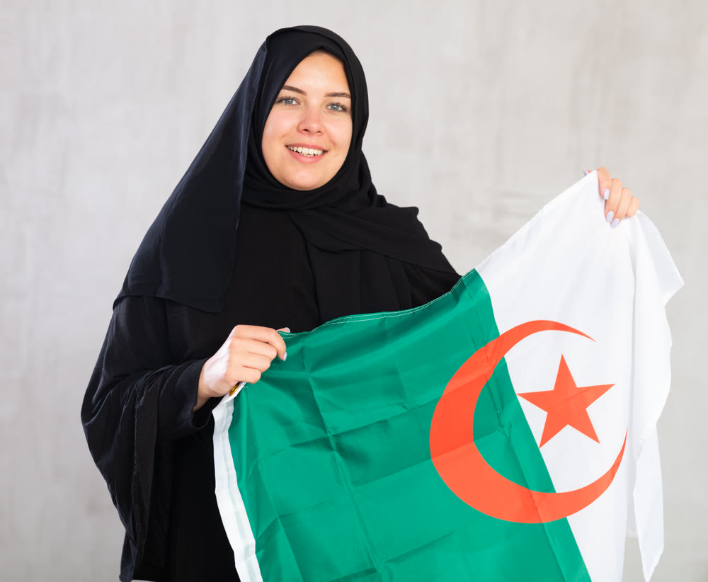Happy young woman dressed in traditional islamic clothes with algerian flag