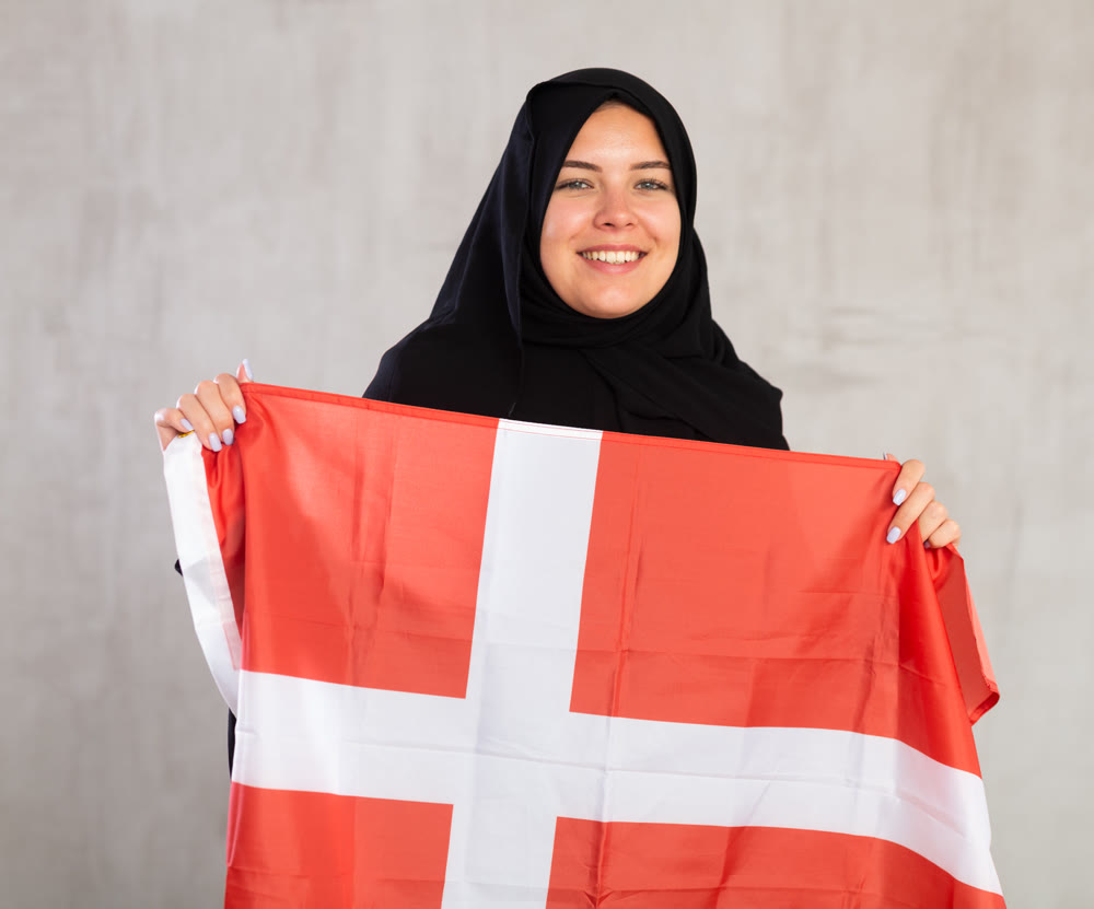 Happy young woman dressed in traditional islamic clothes with danish flag