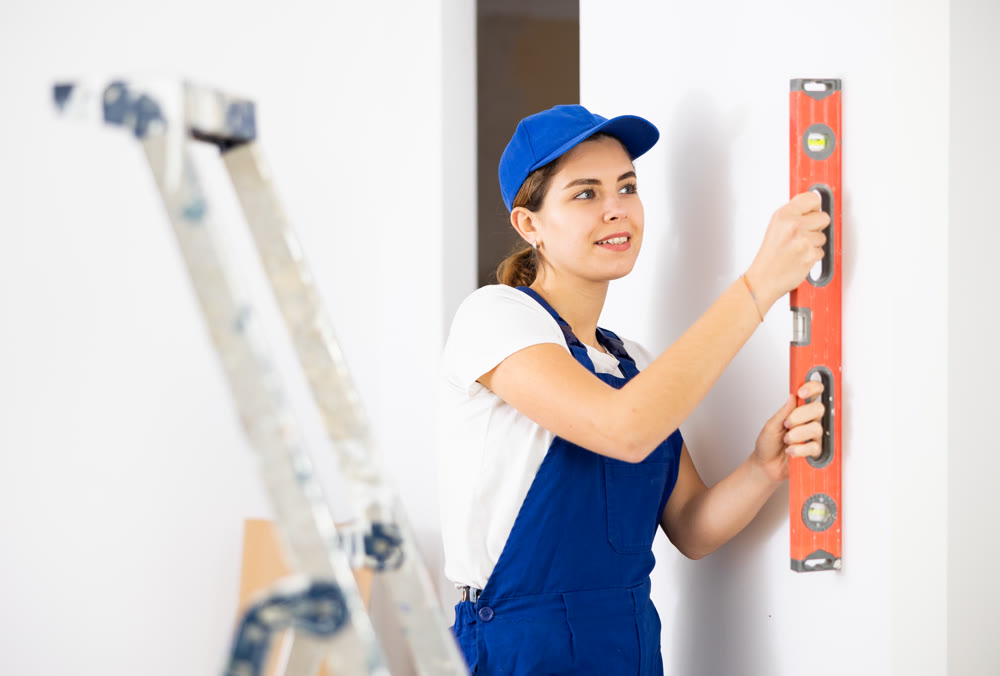 Woman builder using building level measures the vertical of wall