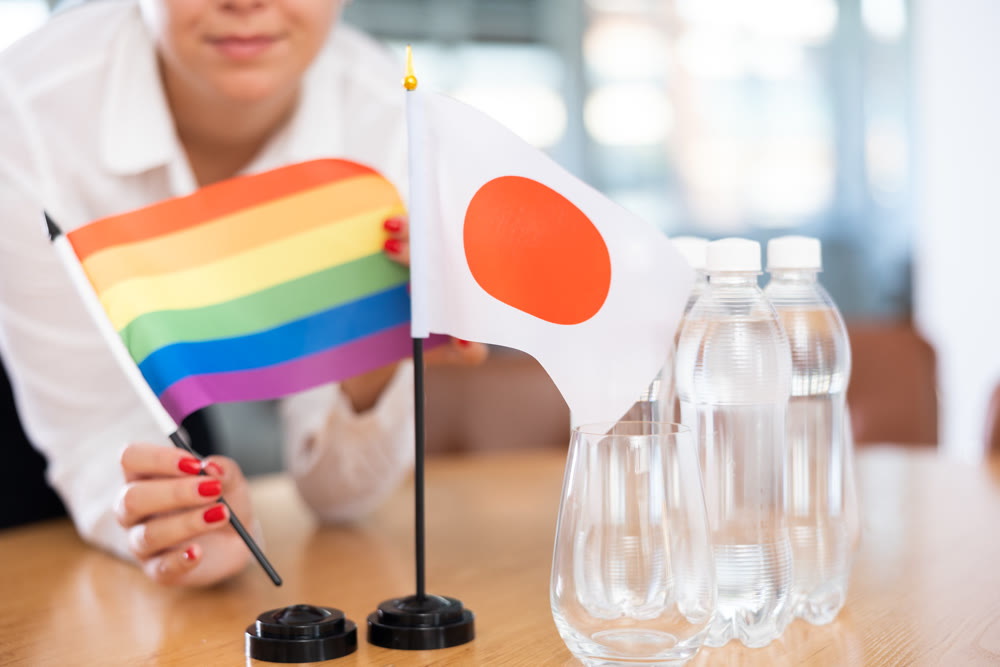 Rainbow flag and flag of Japan in female hands on negotiating table
