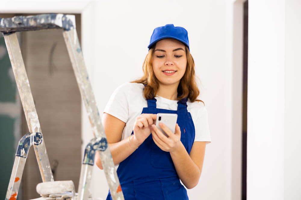 Positive young female contractor chatting online on smartphone