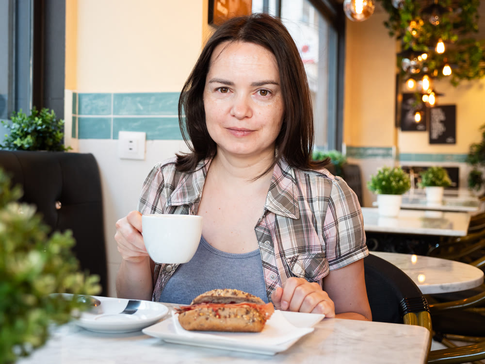 Young woman ordered breakfast - cup of coffee and sandwich with sausage products