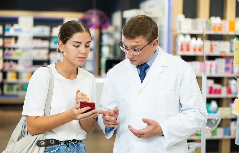Young girl showing to male pharmacist something displayed on her smartphone
