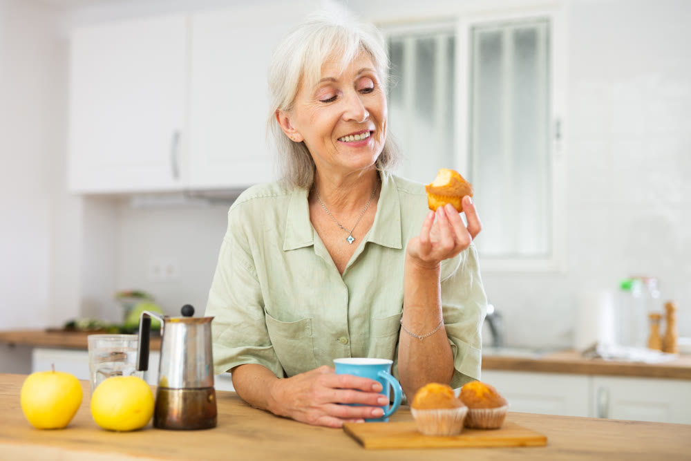 Relaxed elderly woman drinking coffee with muffin