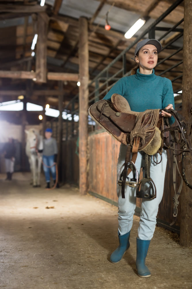Female rancher carrying horse tack and saddle in horse farm
